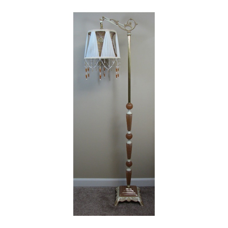 May include: A vintage floor lamp with a white and gold shade and a brown and white base. The shade has a beaded fringe and the base has a decorative design.