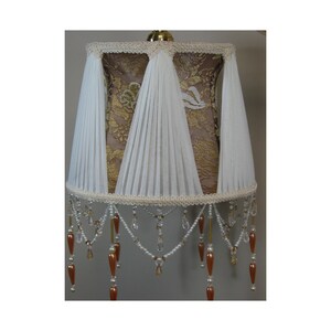 May include: A lampshade with a brown lace base and white pleated fabric overlay. The shade has a beaded fringe with clear and amber beads.