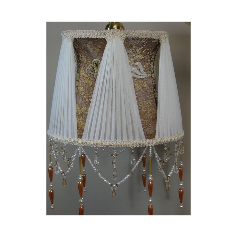 May include: A lampshade with a brown lace base and white pleated fabric overlay. The shade has a beaded fringe with clear and amber beads.