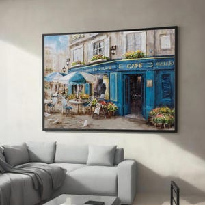 May include: A painting of a Parisian cafe with blue doors and windows, a sign that reads "Cafe en Ville", and tables and chairs set up outside. There are flowers in pots and a sign that reads "Cafe" above the door.