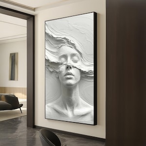 Könnte beinhalten: Weißes Relief einer Frau mit geschlossenen Augen und fließendem Haar. Das Kunstwerk ist in Schwarz gerahmt und an einer Wand montiert, was einen auffälligen visuellen Kontrast erzeugt. Das Stück ist ein modernes Kunstwerk.