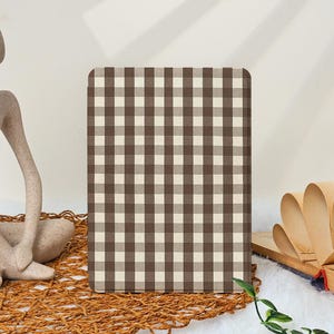 May include: A rectangular notebook or journal with a brown and cream gingham pattern. The cover has a classic checkered design. The item is displayed on a woven mat with a neutral background, suggesting a rustic or farmhouse aesthetic.
