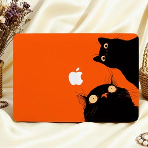 May include: A rectangular laptop skin featuring a vibrant orange background with two black cat illustrations. One cat is positioned at the top right and the other at the bottom right, both with wide eyes. A white Apple logo is centred on the skin.