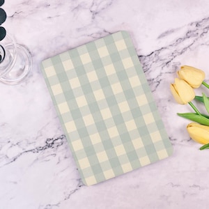 Peut inclure: Un carnet à carreaux bleu clair et crème sur une surface en marbre blanc avec un bouquet de tulipes jaunes.