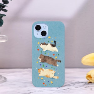 Op de afbeelding: Lichtblau telefoonhoesje met een grillige illustratie van drie katten in verschillende kleuren. De katten worden afgebeeld in een ontspannen pose, met kleurrijke harten en sterren. De hoes heeft een uitsparing voor een dubbele camera.