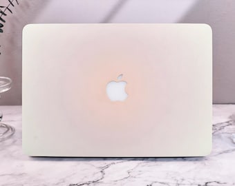 May include: A white laptop computer with a silver Apple logo on the lid. The laptop is sitting on a white marble surface.