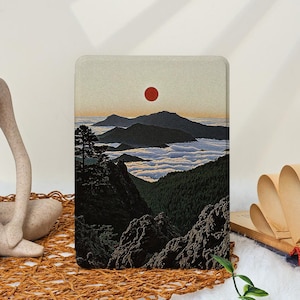 May include: A rectangular art print featuring a mountain landscape with a red sun. The scene depicts dark mountains, a sea of clouds, and a silhouetted tree. The color palette includes shades of black, green, and orange.