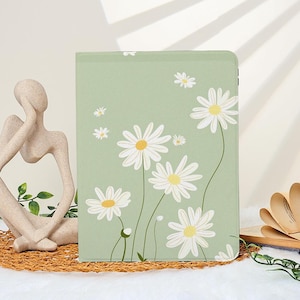 Puede incluir: Una funda para tableta de color verde claro con un estampado floral de margaritas. Las margaritas blancas tienen centros amarillos y tallos verdes. El diseño presenta margaritas de varios tamaños. La funda es rectangular.