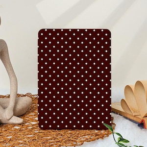Może przedstawiać: Prostokątny przedmiot z zaokrąglonymi rogami, z ciemnobordowym tłem pokrytym wzorem małych, równomiernie rozmieszczonych białych kropek. Przedmiot jest prezentowany na tkanej powierzchni.