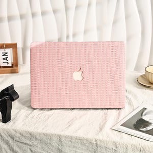 May include: Pink laptop case with a woven texture and the Apple logo in the center.