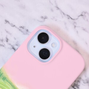 May include: A pink phone case with a clear camera lens cutout. The case has a subtle design of a green field with a light blue sky.