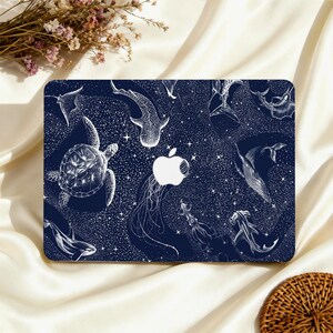 May include: A navy blue laptop case featuring a white illustration of various sea creatures, including a turtle, whale shark, and jellyfish. The design includes a white Apple logo and a starry background.