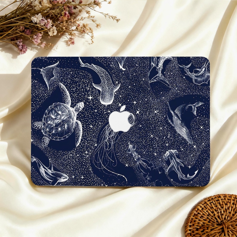 May include: A navy blue laptop case featuring a white illustration of various sea creatures, including a turtle, whale shark, and jellyfish. The design includes a white Apple logo and a starry background.