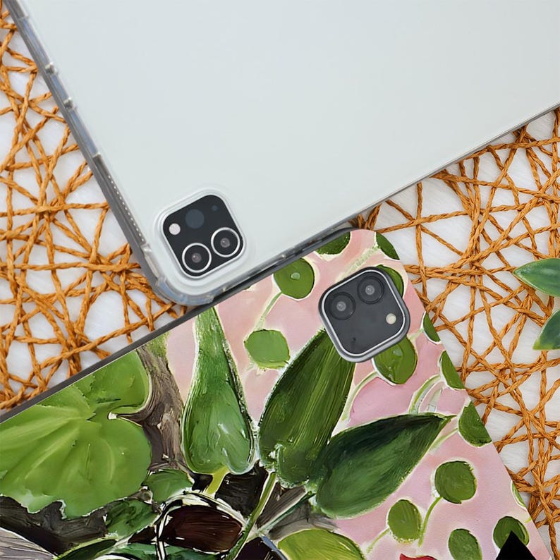 May include: Two tablet cases. One is clear, the other features a floral design with green leaves and pink background. The cases are on a woven, tan surface. The tablet cameras are visible.