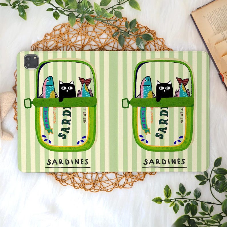 May include: A light green striped tablet case featuring two sardine cans with a black cat and colorful fish. The cans are labeled "Sardines" and "In Olive". The case has a whimsical, cartoon-like design.