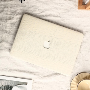 May include: A white laptop case with a crocodile skin pattern. The case has a white Apple logo on the front.
