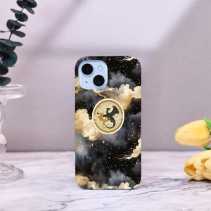 Könnte beinhalten: Eine schwarze Smartphone-Hülle mit einem goldenen und schwarzen Drachendesign. Die Hülle hat einen schwarzen und goldenen Wolkenhintergrund mit einem kreisförmigen Drachenemblem. Die Handyhülle ist ein schützendes Zubehör.