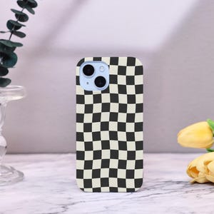 Può includere: Una custodia per telefono con un motivo a scacchiera bianco e nero. La custodia ha una forma rettangolare arrotondata con un ritaglio per la fotocamera nella parte superiore. La custodia del telefono è un accessorio elegante.