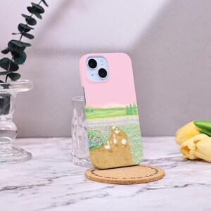 May include: A pink phone case with a landscape scene of a field with ducks walking on a path. The case has a camera lens cutout and a white background.