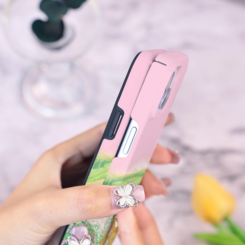 May include: A pink and black phone case with a floral design. The case has a raised edge around the camera lens.