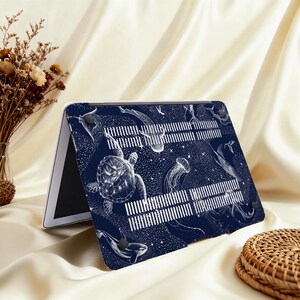 May include: A navy blue laptop case featuring a white illustration of various sea creatures, including a turtle, jellyfish, and whales. The design includes a starry background and white vertical lines.