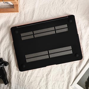May include: Black laptop case with a textured surface and a pink trim. The case has a series of small holes for ventilation.