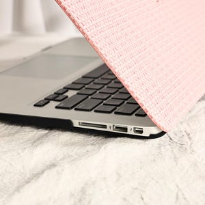 May include: A pink laptop sleeve with a textured woven design. The sleeve is covering a silver laptop with a black keyboard.