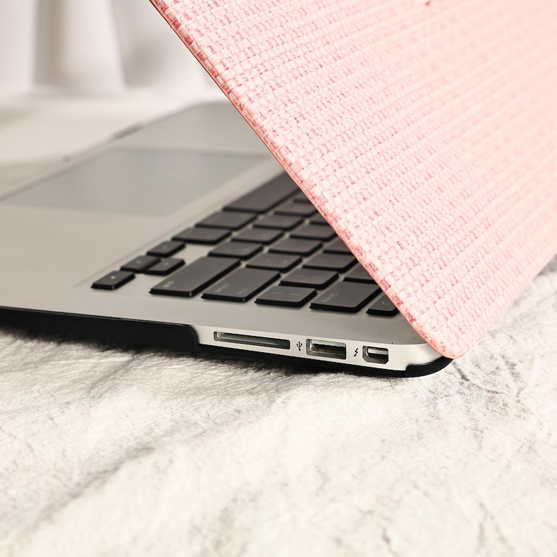 May include: A pink laptop sleeve with a textured woven design. The sleeve is covering a silver laptop with a black keyboard.