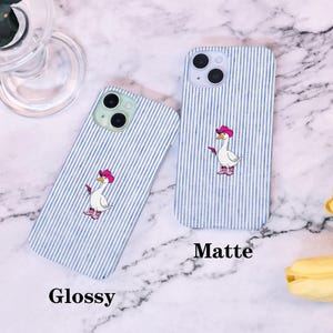 Może przedstawiać: Dwa etui na telefon z niebiesko-białym wzorem w paski. Jedno etui jest oznaczone jako "Glossy", a drugie jako "Matte". Każde etui przedstawia kresk&oacute;wkową gęś w r&oacute;żowym kapeluszu kowbojskim i butach, trzymającą pistolet.