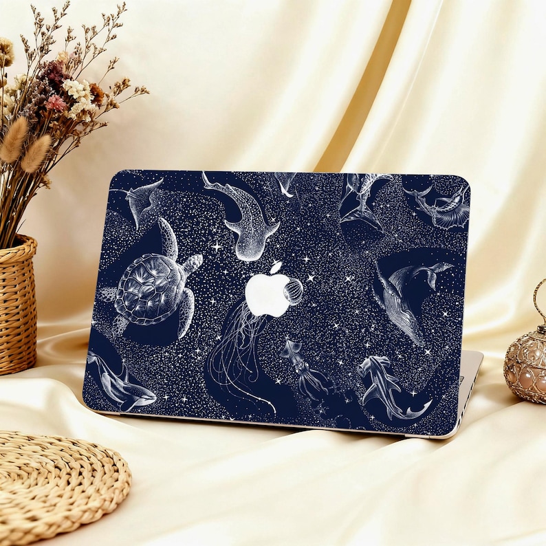 May include: A navy blue laptop case featuring a white illustration of various marine animals, including a sea turtle, whale shark, and jellyfish. The design is set against a starry background, with the Apple logo visible.