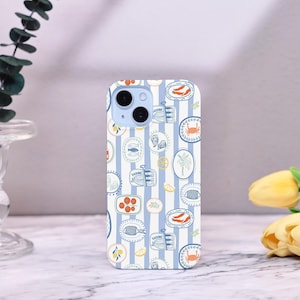 以下が含まれることがあります： 青と白のストライプの背景に、イワシ、カキ、カニなどのシーフードのイラストが繰り返されるパターンの携帯電話ケース。ケースには水色のカメラモジュールが付いています。