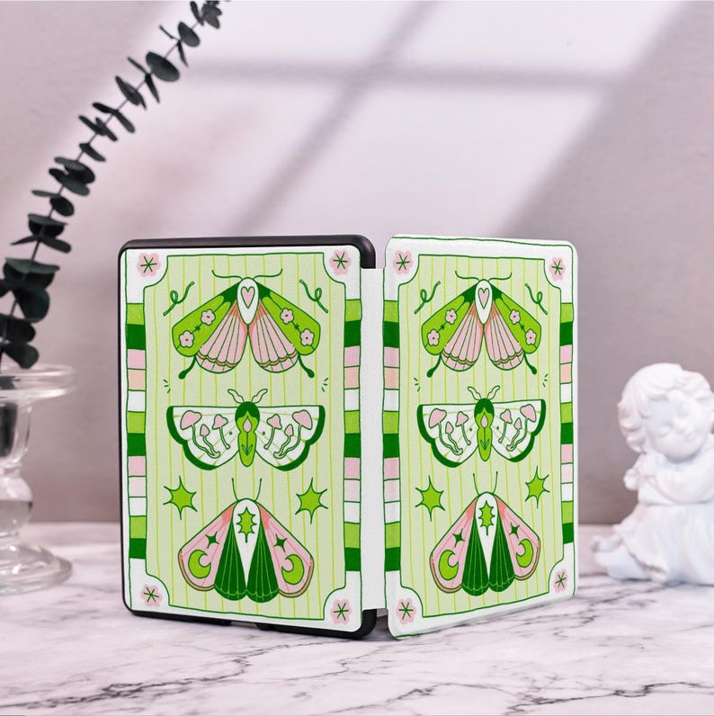 May include: A green and pink book cover with a butterfly design. The cover is divided into two sections, each with a different butterfly pattern. The butterflies are surrounded by green and pink flowers and leaves.