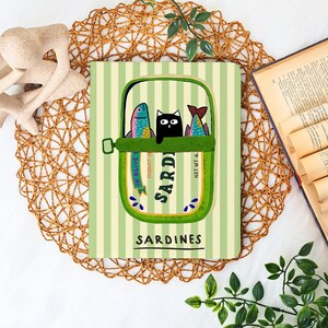 May include: Notebook with a whimsical sardine can design. The illustration features a black cat peeking out between two colorful fish inside a green can, set against a striped background. The word "Sardines" is printed below.