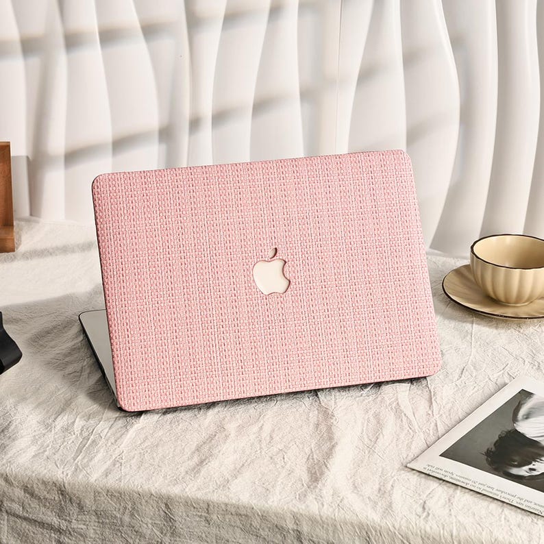 May include: A pink laptop case with a textured fabric design and a silver Apple logo. The case is on a white surface.