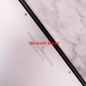 以下が含まれることがあります： シルバーのMacBookの底面のクローズアップ。テキストには「Designed by Apple in California」と「Model A1406」が含まれています。ラップトップには黒い縁と規制記号があります。