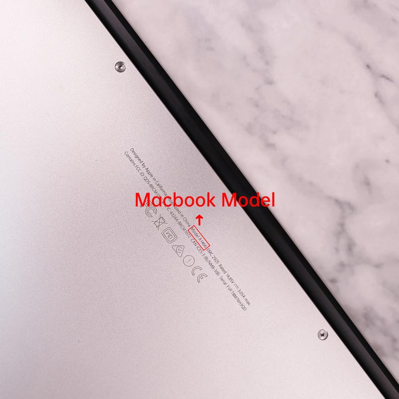 以下が含まれることがあります： シルバーのMacBookの底面のクローズアップ。テキストには「Designed by Apple in California」と「Model A1406」が含まれています。ラップトップには黒い縁と規制記号があります。
