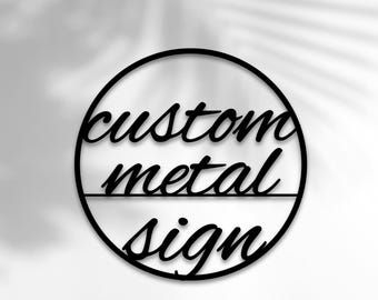 Può includere: Un cartello circolare in metallo nero con il testo "custom metal sign" in un font corsivo.