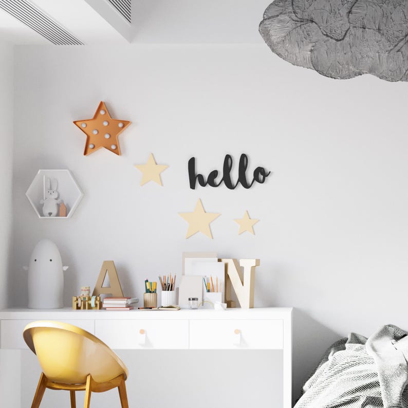 May include: A white desk with two drawers and a yellow chair. The wall behind the desk has a black wooden sign that says "hello" and several wooden stars. There is a white ghost-shaped lamp on the desk.