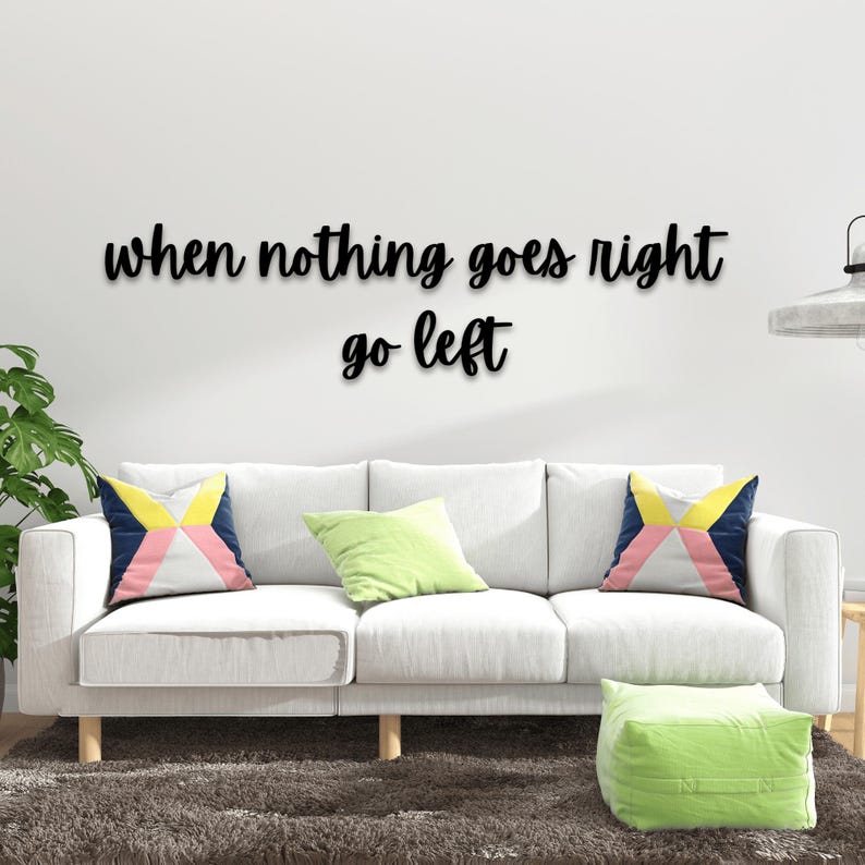 May include: White couch with three pillows, a green ottoman, and a black wall sign that reads "when nothing goes right go left".