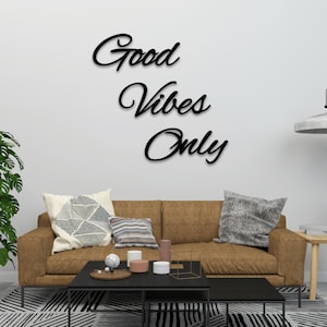 May include: A brown leather sofa with pillows and a black coffee table in front of it. The wall behind the sofa has a black wooden sign that reads "Good Vibes Only".