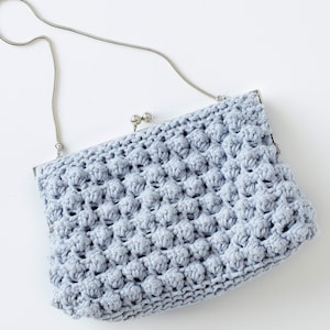 Puede incluir: Un bolso de mano de crochet azul claro con una correa de cadena plateada.