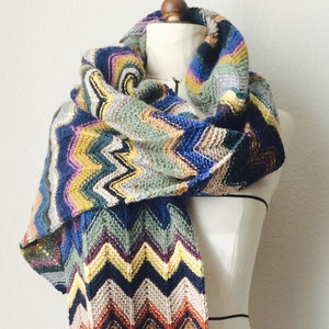 May include: A colorful chevron patterned scarf in shades of blue, green, yellow, orange, and brown. The scarf is draped over a white dress form.