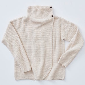 May include: A cream-colored waffle knit sweater with a mock neck and a single button closure on the shoulder.