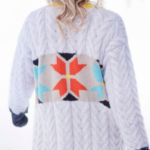 Könnte beinhalten: Weißer Strickcardigan mit geometrischem Muster in Orange, Blau und Beige auf der Rückseite. Der Cardigan hat ein Zopfmuster und eine lange, lockere Passform.