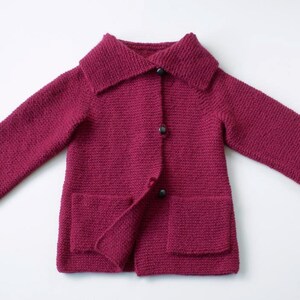 Könnte beinhalten: Ein burgunderfarbener Strickcardigan mit großem Kragen, drei Knöpfen und zwei Taschen.