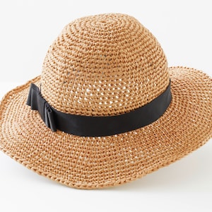 May include: A brown straw hat with a wide brim and a black ribbon around the crown. The hat is made of a woven material and has a delicate texture.