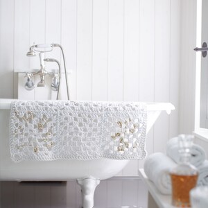 Könnte beinhalten: Eine weiße Badewanne mit Krallenfüßen und einer gehäkelten weißen Badematte mit goldenen Akzenten. Die Badewanne befindet sich in einem weißen Badezimmer mit weißen Holzverkleidungen.