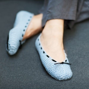 Könnte beinhalten: Hellblaue gestrickte Ballerinas mit schwarzen Akzenten. Die Ballerinas haben eine kleine schwarze Schleife auf der Oberseite und eine runde Spitze. Die Schuhe sind aus einem weichen, strukturierten Material gefertigt und für den Innenbereich geeignet. Ca. 23 cm lang.