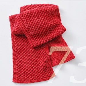 May include: A bright red, hand-knitted scarf with a textured bobble stitch pattern. The scarf is folded, displaying its length and the detailed craftsmanship. The vibrant colour and unique texture make it a standout accessory.