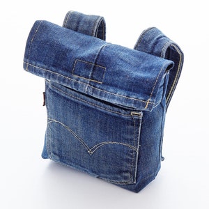 May include: A blue denim crossbody bag with a flap closure and a large pocket on the front. The bag has adjustable straps and a zipper closure.